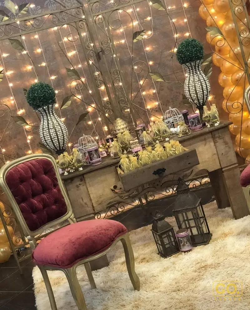 Canto decorado com cortina de luzes, console de madeira com lembrancinhas, poltrona de veludo e tapete felpudo.