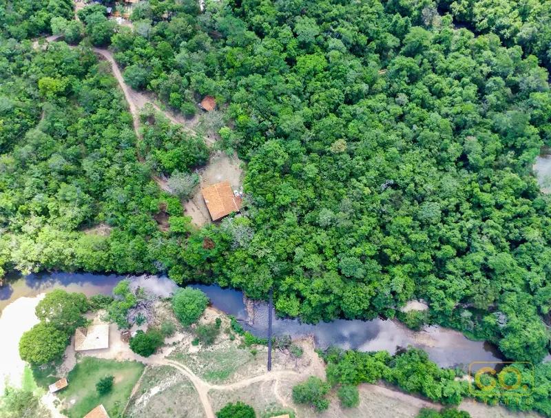 Vista aérea de casas de telhado de barro às margens de um rio sinuoso cercado por densa mata verde.