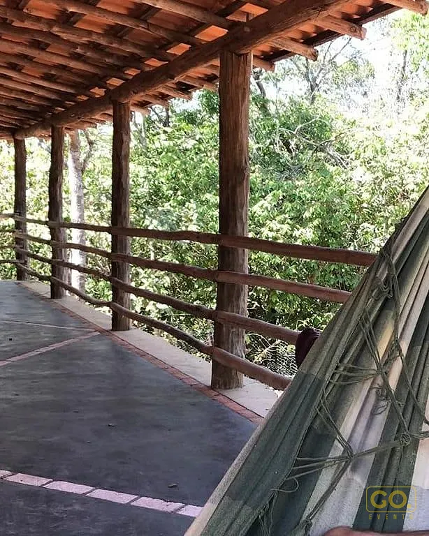 Varanda rústica coberta com pilares de madeira, guarda-corpo de toras e rede estendida, com vista para a mata verde.