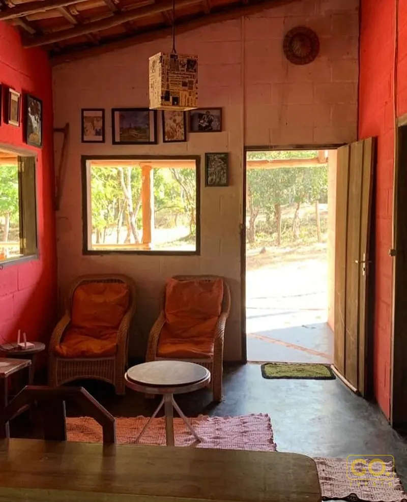 Sala rústica de paredes vermelhas com duas poltronas de vime e porta aberta para a vegetação externa.