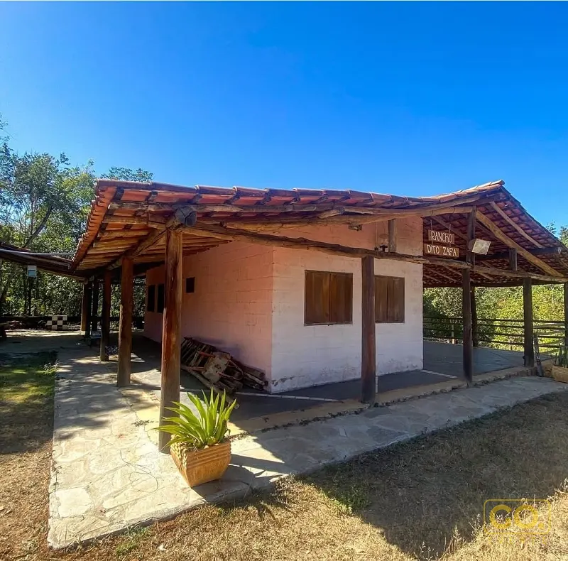 Varanda coberta de um rancho rústico com paredes rosadas, telhado de telha e pilares de madeira sob céu azul.