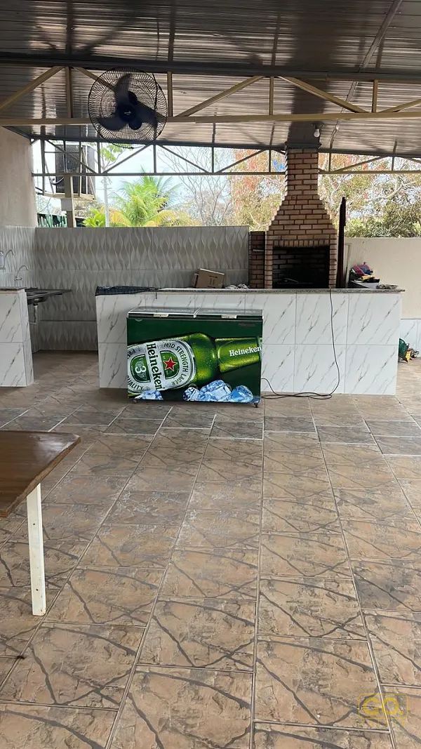 Área coberta com churrasqueira de tijolos aparentes, bancada revestida de azulejo e cooler de cerveja, sem pessoas nem evento.