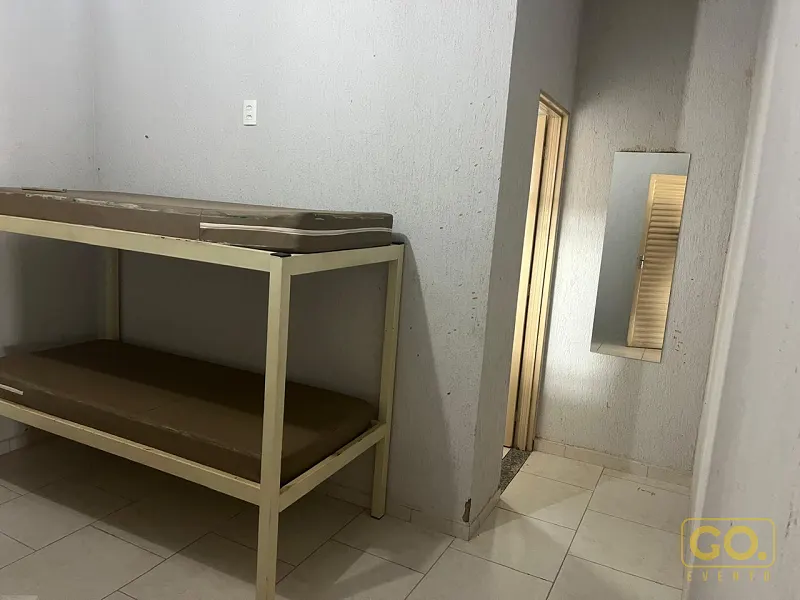Cômodo pequeno de paredes brancas com beliche de metal, piso cerâmico claro e nicho com espelho ao lado de uma porta.