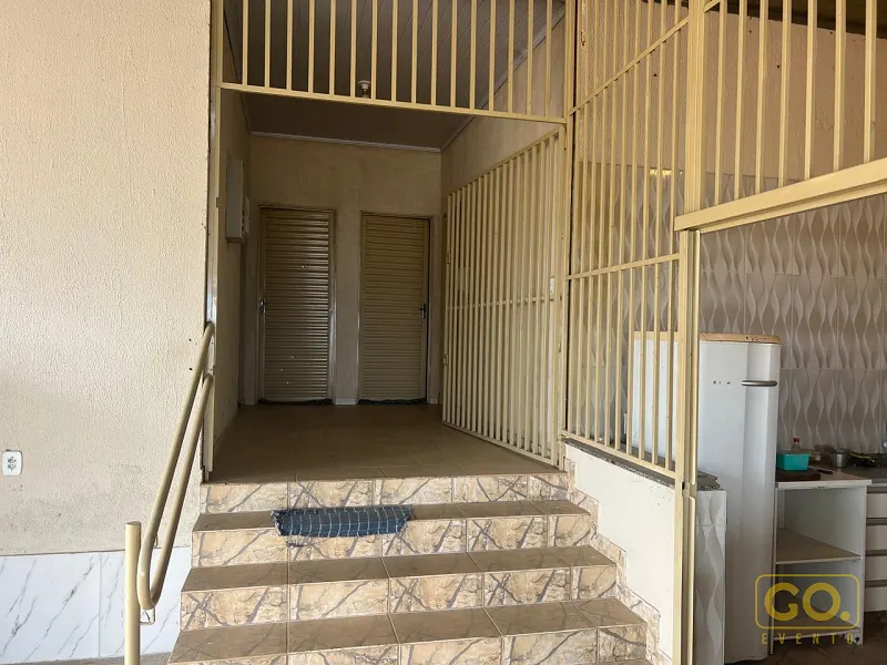 Escada revestida de cerâmica leva a um corredor com duas portas de enrolar metálicas e, à direita, uma cozinha com geladeira branca.