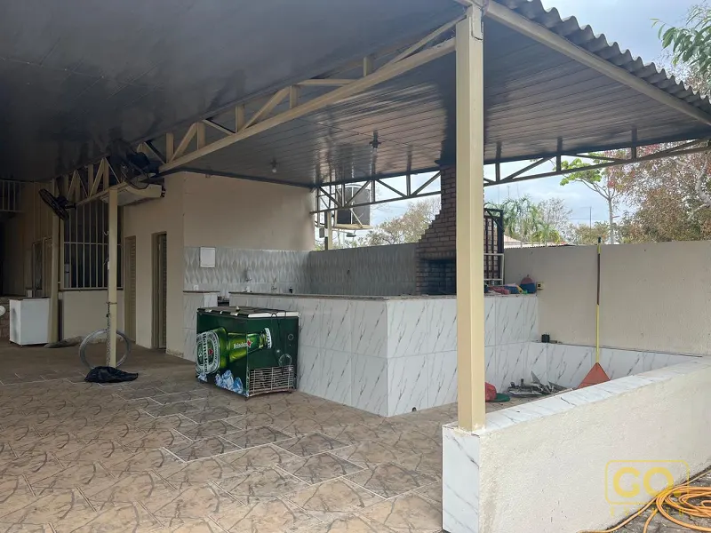 Área coberta com churrasqueira de tijolos e balcão revestido em mármore, piso de cerâmica e sem pessoas à vista.