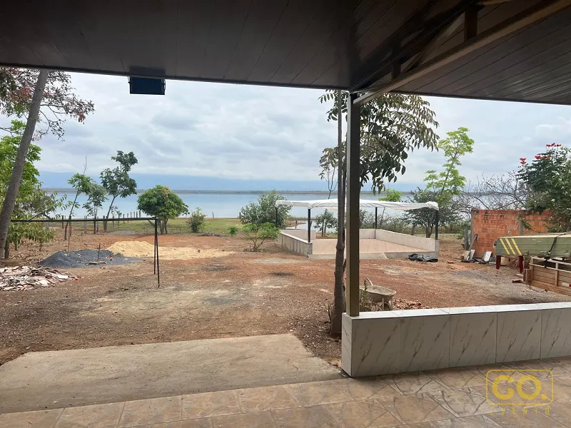 Varanda coberta com piso de cerâmica voltada para terreno de terra e lago ao fundo, sem montagem de evento.