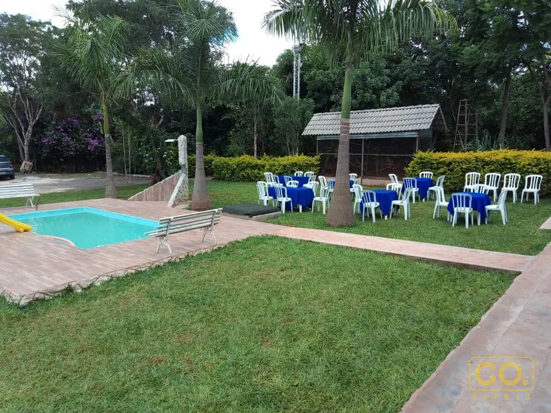 Gramado com piscina pequena, deck de madeira e mesas redondas com toalhas azuis e cadeiras brancas montadas ao ar livre.