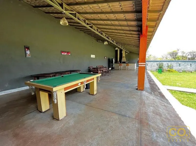 Área coberta com mesa de sinuca de feltro verde, churrasqueira de alvenaria ao fundo e gramado ao lado.