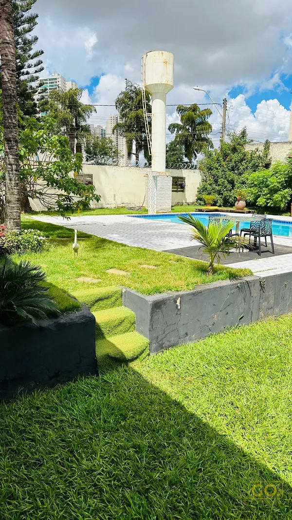 Gramado bem cuidado em primeiro plano, com degraus de grama, piscina azul ao fundo e caixa d'água sobre o muro do quintal.